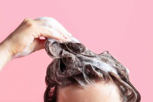 a-girl-washes-her-hair-with-shampoo-on-a-pink-background-front-view