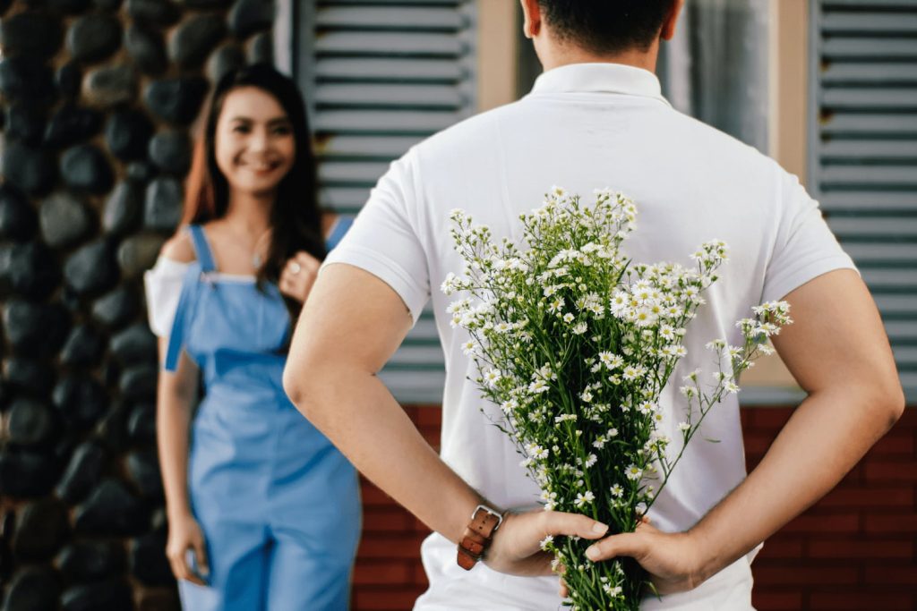 Man with a crush on a woman, hiding flowers behind his back