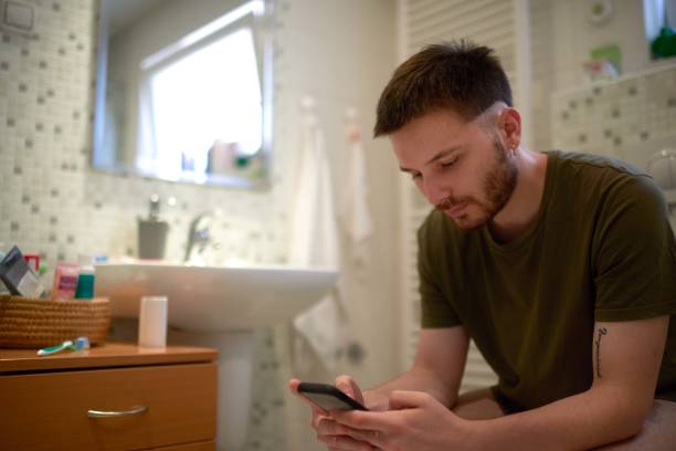 young-gay-male-person-sitting-on-the-toilet-and-using-mobile-phone