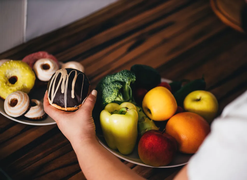 woman-reaching-for-junk-dessert-sweets-over-vegetables