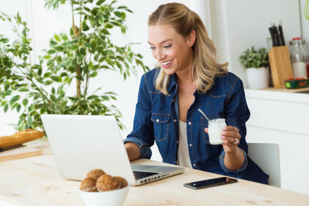 portrait-of-beautiful-young-woman-using-her-laptop-and-eating-yogurt-at-home