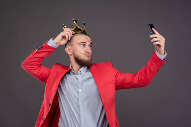 young-bearded-handsome-man-in-gold-crown-taking-selfie-looking-at-smartphone