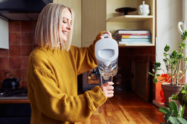 smiling-mature-woman-pouring-filtered-water-into-glass-at-kitchen
