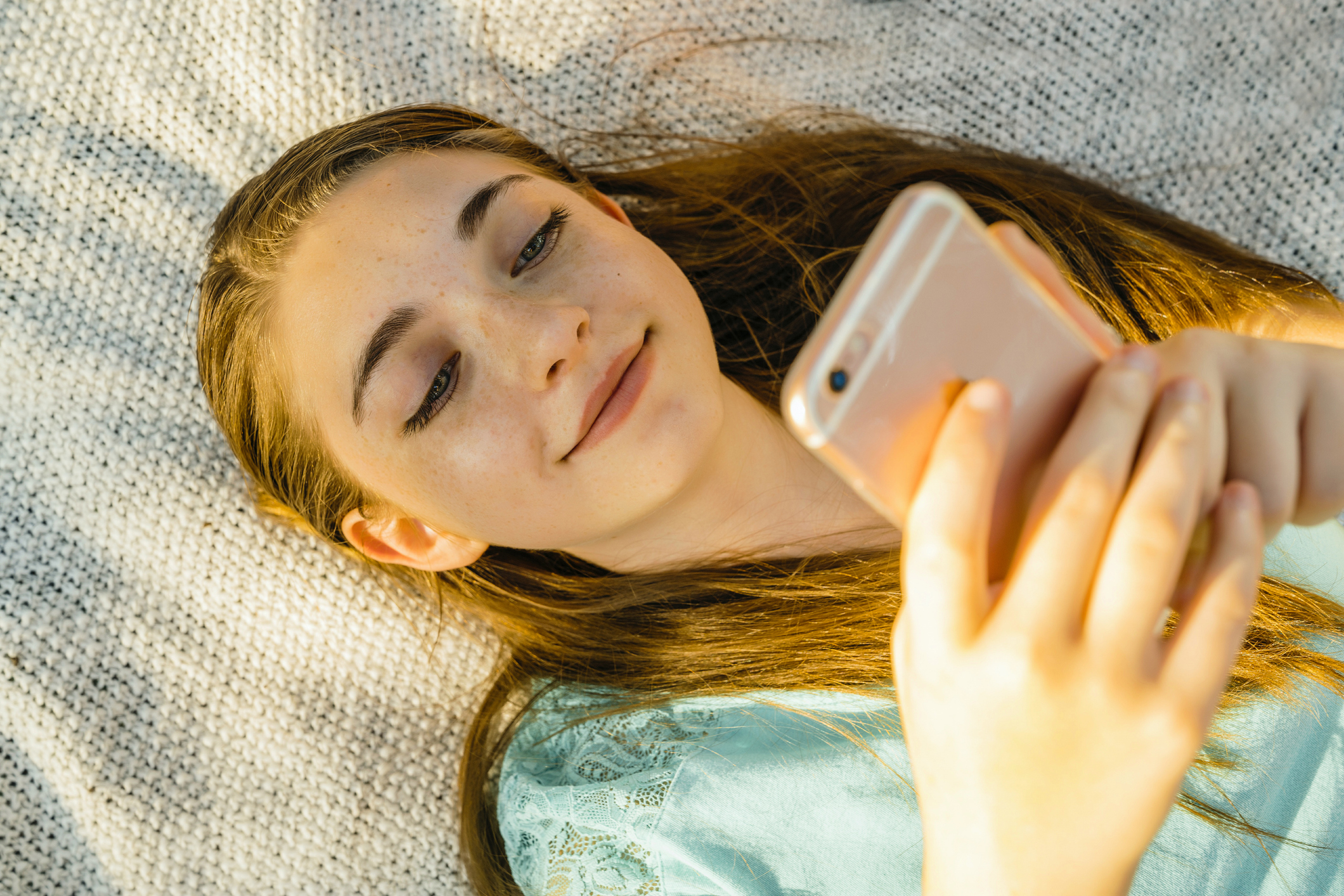caucasian-girl-laying-on-blanket-texting-on-cell-phone